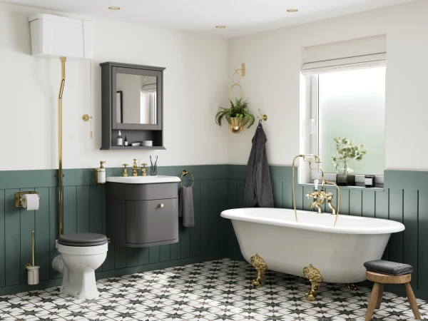 White freestanding claw-foot tub with brass feet and taps, dark grey vanity, green wainscoting, black-and-white patterned floor, and frosted window.