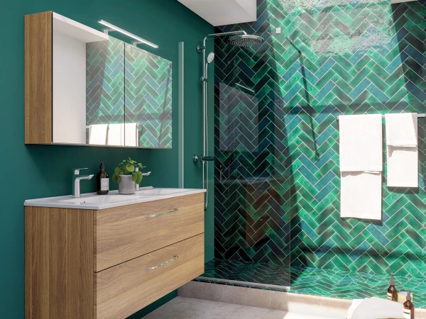 Teal walls with a wooden floating double-drawer vanity, a wide mirror, and a glass-walled shower with green herringbone tile; skylight overhead and towels on a rack.