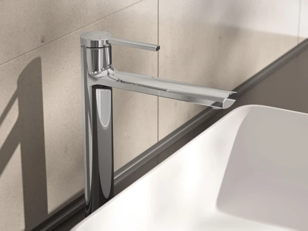 Chrome single-lever tap with a long horizontal spout beside a white rectangular sink, mounted on a dark countertop against a beige tiled wall.