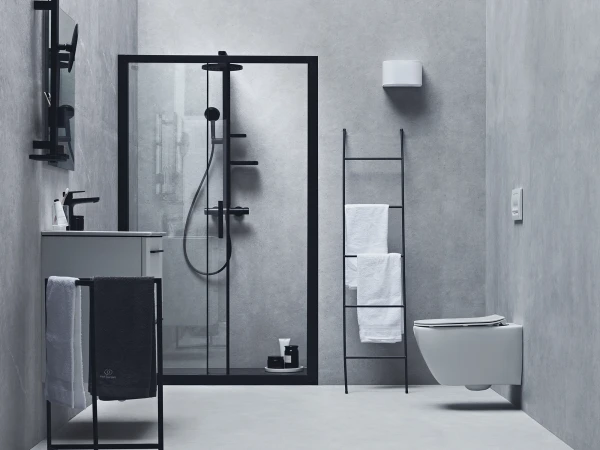 Minimalist grey bathroom with a glass-framed shower, black fixtures, a wall-mounted sink, and a ladder towel rack beside a wall-hung toilet.