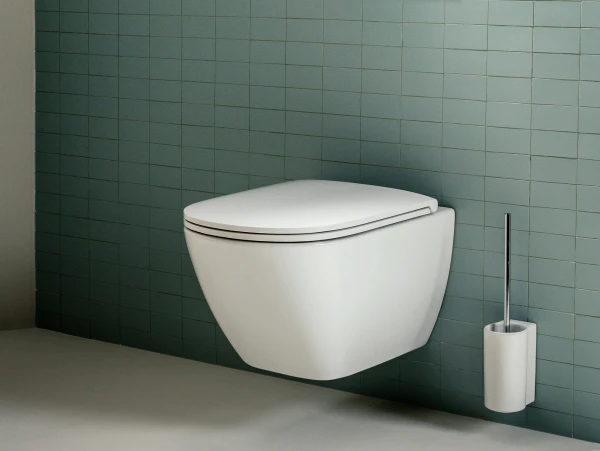 Modern wall-mounted white toilet against teal tiled wall, with a rectangular flush plate above and a toilet brush holder to the right.