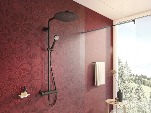 Modern bathroom with black matte rainfall and handheld shower on burgundy floral wall, glass partition, towel rail, and a stool by a window.