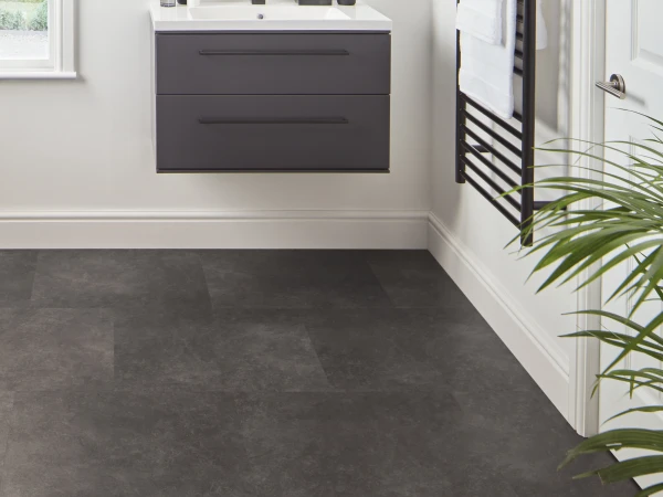Modern bathroom with a floating dark grey vanity, white sink, round mirror, industrial wall lights, window with blind, black towel rail with white towels, and dark tiled floor.