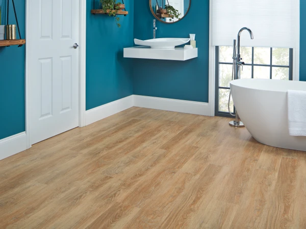 Teal bathroom with a white freestanding bathtub by a window, a floating white sink with circular mirror, wooden shelves with plants, white door and light wood floor.