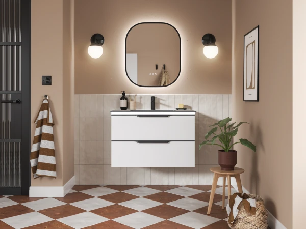 Modern peach bathroom with a wall-mounted white double-drawer vanity beneath a rounded backlit mirror; two globe lights, striped towel, plant on a stool, checkered floor.