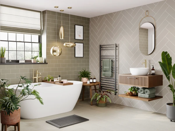 Modern bathroom with a white freestanding tub, beige herringbone wall, gold fixtures, a wooden vanity with basin, round mirror, towel rail and plants.
