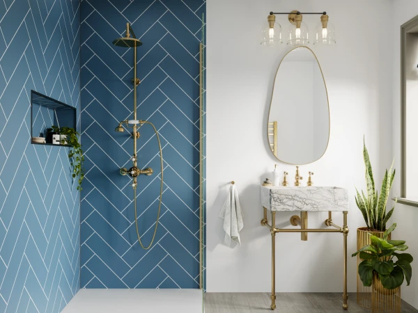 Bathroom with blue herringbone shower tiles and brass fixtures, marble-topped vanity, oval mirror, three-globe light, and potted plants.