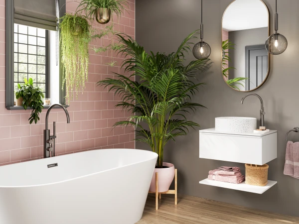 Bright bathroom with a white freestanding tub beside a pink tiled wall and grey accent wall, hanging plants, an oval mirror, and a floating sink on wood flooring.