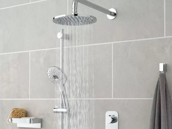 Modern shower setup featuring a ceiling rainfall head and a handheld sprayer on a vertical bar; grey tiled wall, towel on a rail, and a sponge on a shelf.