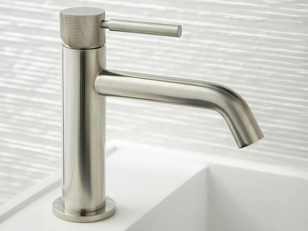 Polished stainless-steel single-handle faucet with a knurled top cap and curved spout, mounted on a white sink.