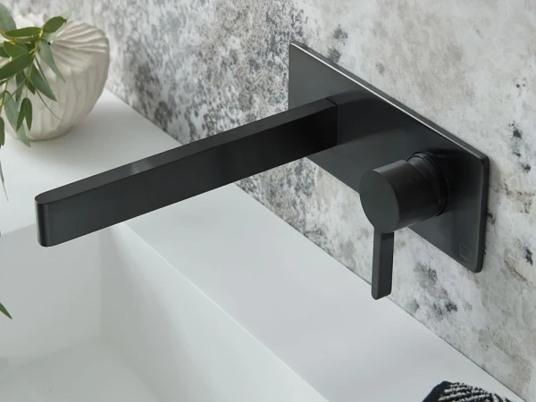 Matte black wall-mounted bathroom faucet with a long rectangular spout and vertical lever on a square backplate above a white sink.