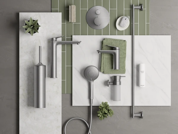 Flat lay of modern bathroom fixtures on marble slabs with sage-green tiles: handheld shower, faucet, towel, soap, brush, and plants.
