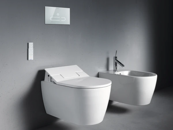 Minimalist bathroom with a wall-mounted white toilet and a floating bidet on a grey concrete wall and floor; slim flush plate and wall controls nearby.