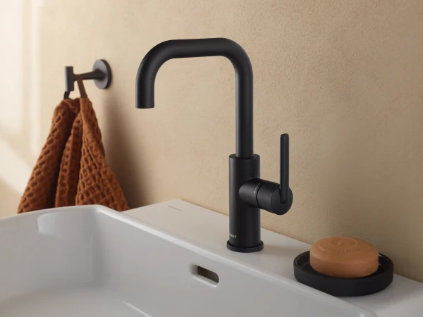 Matte black high-arc bathroom tap over a white sink, with a brown textured towel on the left and a soap dish holding a bar of soap on the right.