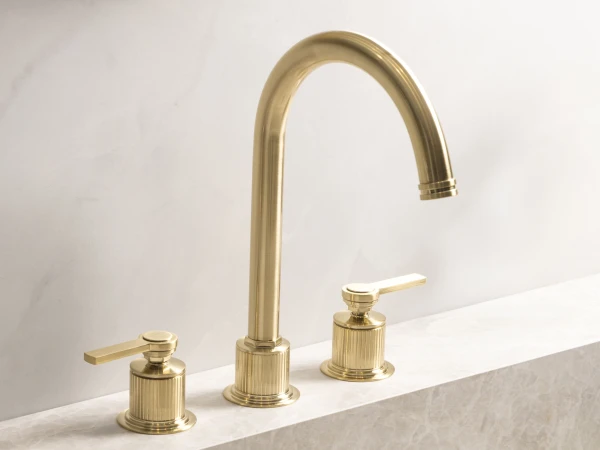 Brass faucet with a tall curved spout and two lever handles, mounted on a marble countertop sink.