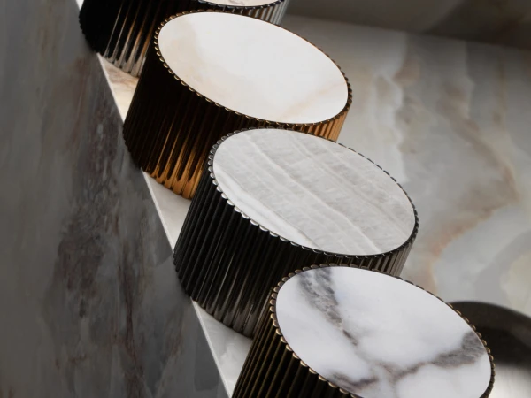 Five round marble-topped cylinders with dark ribbed sides, arranged diagonally along a light marble surface.