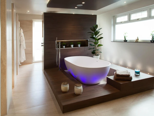 Modern bathroom with a freestanding white tub on a dark wood platform, blue underlighting, a wood-paneled wall, and a bright window sill with small plants.