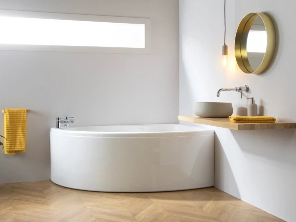Bright, modern bathroom with a white freestanding tub, wooden shelf sink, gold round mirror, pendant light, and yellow towels on a herringbone floor.