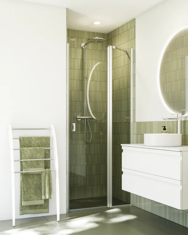 Modern bathroom with glass shower enclosure and olive-green tiles, a round mirror, white vanity and sink, and a white towel rack with green towels.