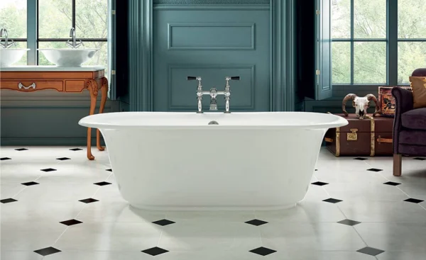 White freestanding bath at centre of teal bathroom with a diamond floor; wooden vanity left and a chair with a vintage trunk and skull on the right.