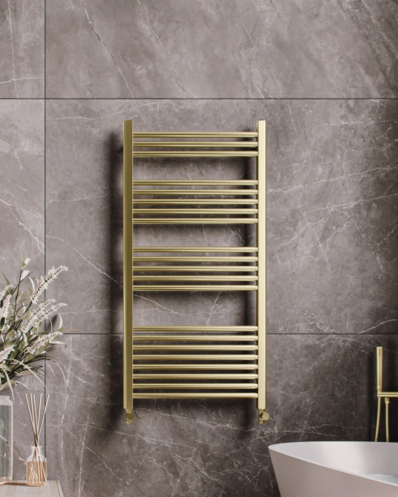 Luxurious bathroom with grey marble walls, a gold ladder towel warmer, a white freestanding tub with gold fixtures, and a vase of white flowers on a wooden surface.