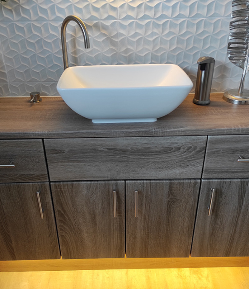 White rectangular vessel sink on a dark wood vanity with a tall curved faucet, blue geometric tiled splashback, and a soap dispenser to the right.